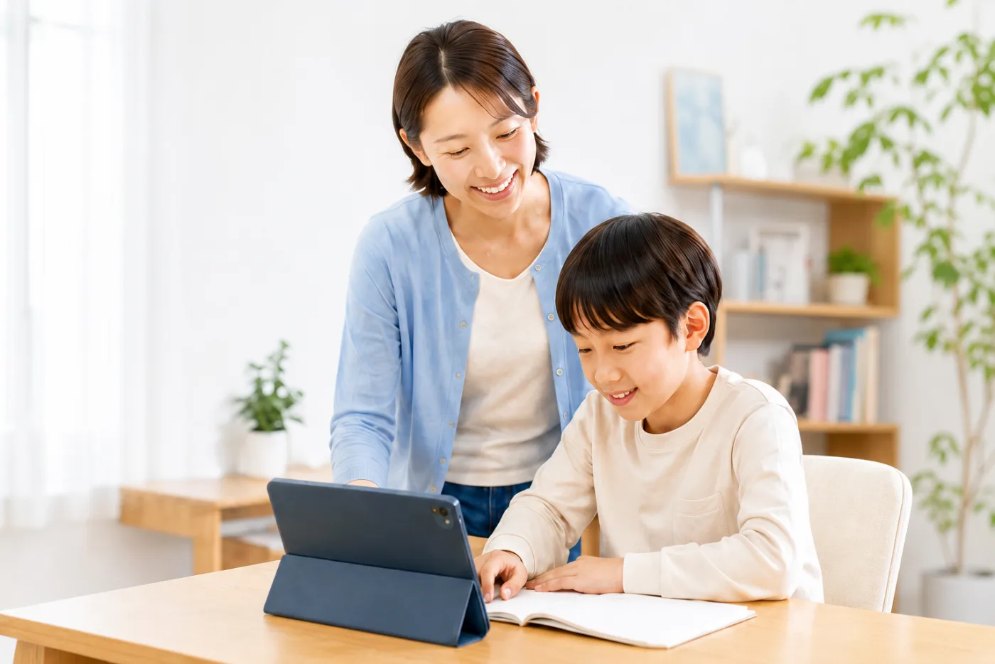 明るい家庭の室内で母親と子どもがタブレットとノートを見ながら学習している写真